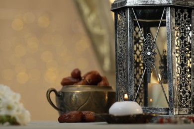 Photo of Arabic lantern, burning candles and dates on table against blurred lights