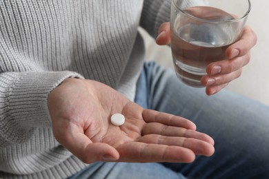 Photo of Man with glass of water and pill on blurred background, closeup