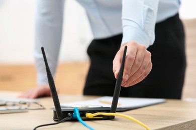 Photo of Man adjusting antenna of Wi-Fi router at wooden table indoors, closeup