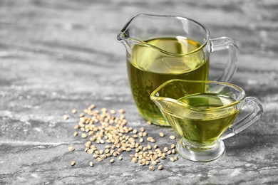 Photo of Glass pitcher and gravy boat with hemp oil on grey table