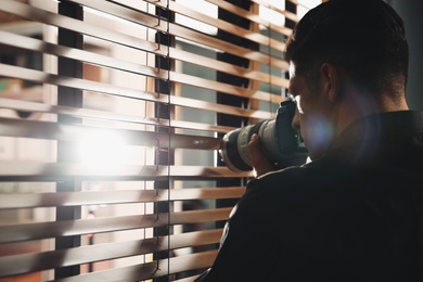 Photo of Private detective with camera spying near window indoors