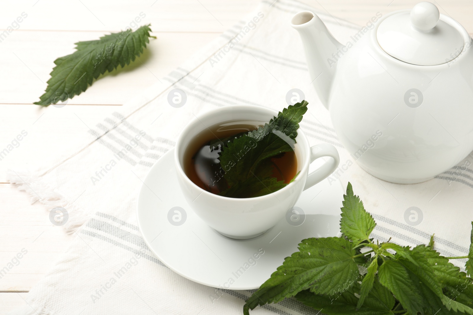 Photo of Aromatic nettle tea and green leaves on white wooden table