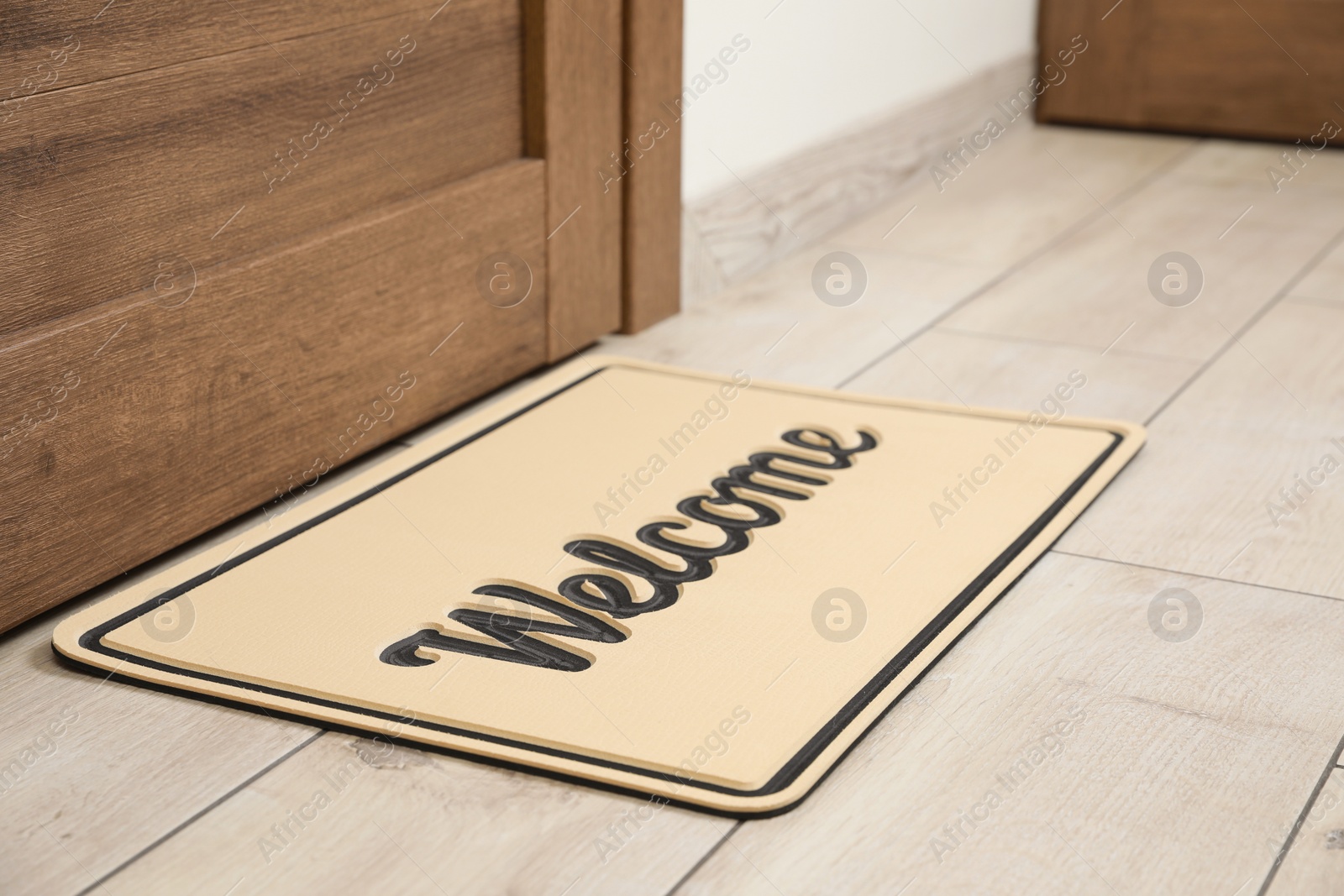 Photo of Beautiful beige doormat with word Welcome on floor near entrance