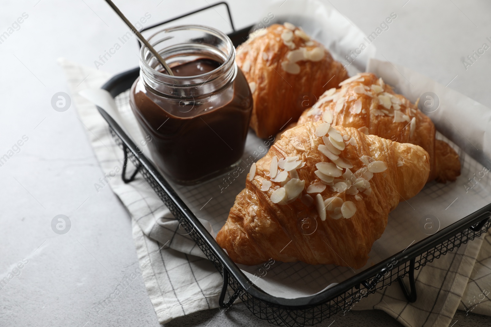 Photo of Delicious croissants with almond flakes and chocolate paste on light grey table, closeup