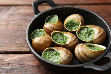 Delicious cooked snails in baking dish on wooden table, closeup