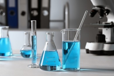 Photo of Different laboratory glassware with light blue liquid on table