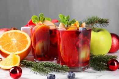 Aromatic Sangria drink in glasses, ingredients and Christmas decor on white marble table
