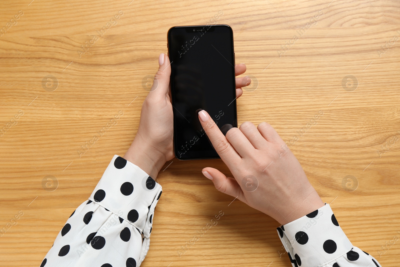 Photo of Woman using smartphone at wooden table, top view