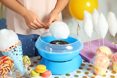 Woman making cotton candy using modern machine at table, closeup