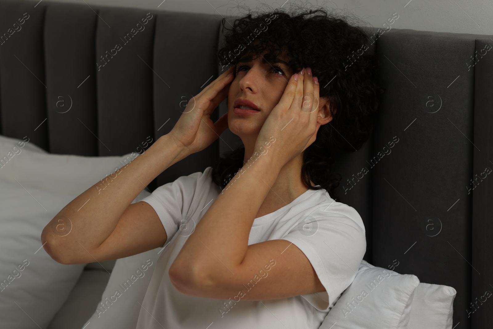 Photo of Young woman suffering from headache in bed at night