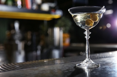 Photo of Glass of martini cocktail with olives on bar counter. Space for text