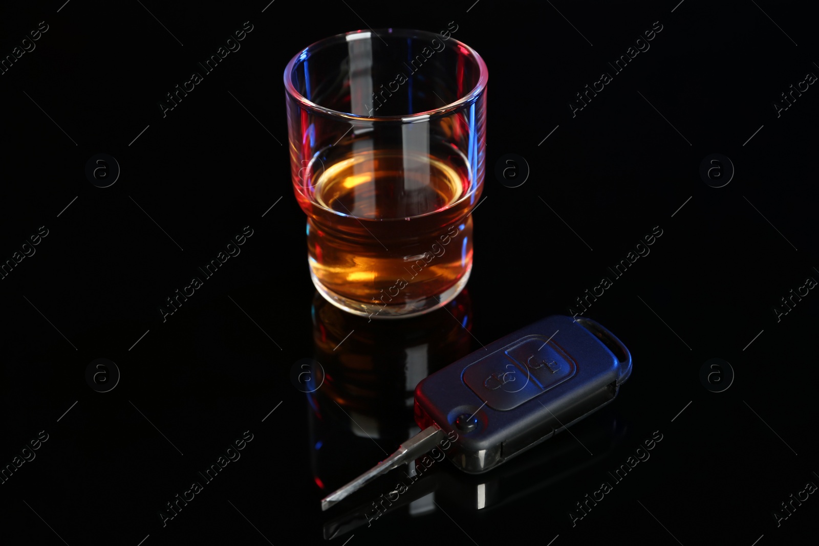 Photo of Car key near glass of alcohol on black table. Dangerous drinking and driving