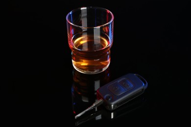 Photo of Car key near glass of alcohol on black table. Dangerous drinking and driving