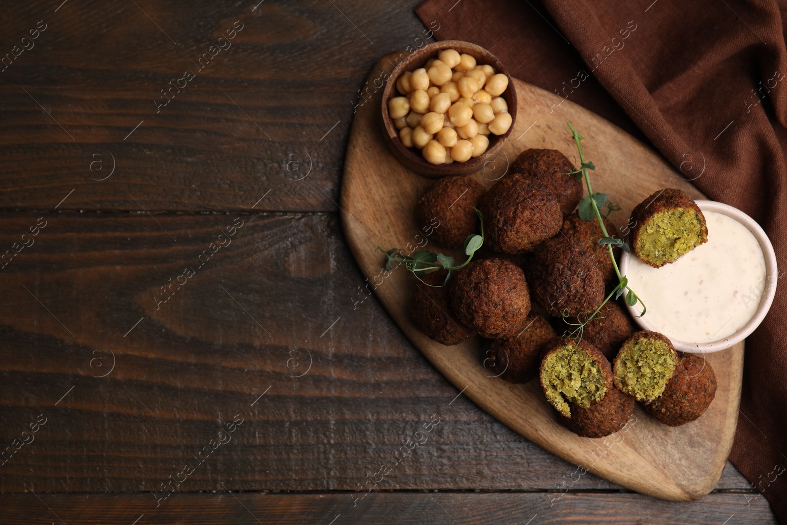 Photo of Delicious falafel balls, chickpeas and sauce on wooden table, top view. Space for text