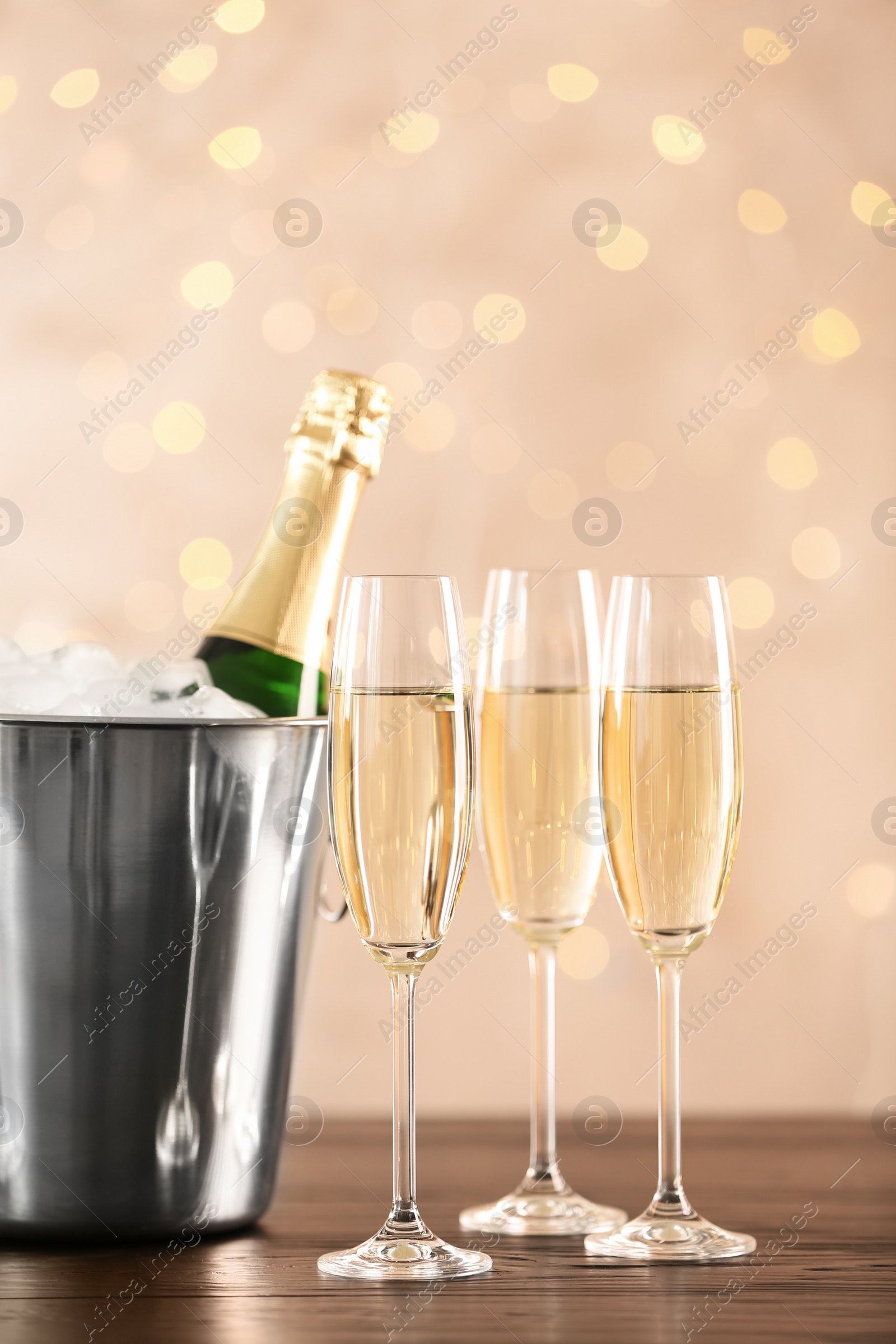 Photo of Glasses with champagne and bottle in bucket on table against blurred lights