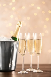 Glasses with champagne and bottle in bucket on table against blurred lights