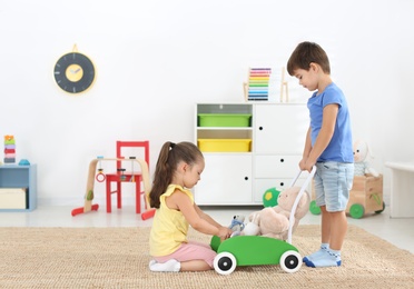 Photo of Cute little children playing with toy walker at home