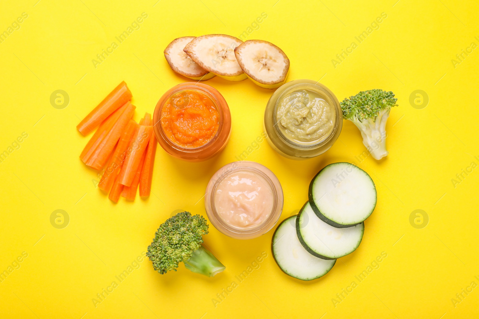 Photo of Glass jars with healthy baby food and ingredients on yellow background, flat lay