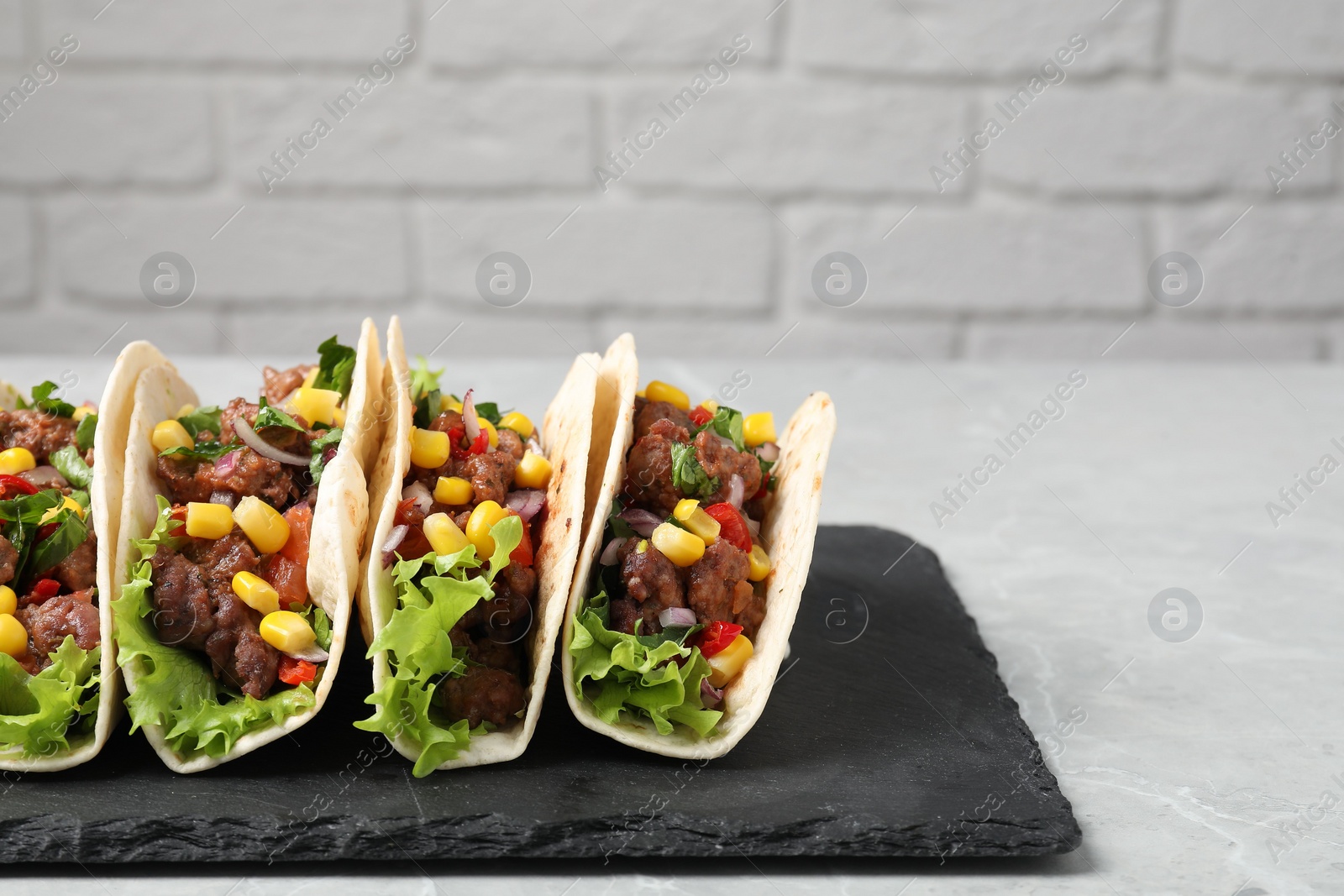 Photo of Delicious tacos with meat and vegetables on light gray marble table against brick wall, closeup. Space for text