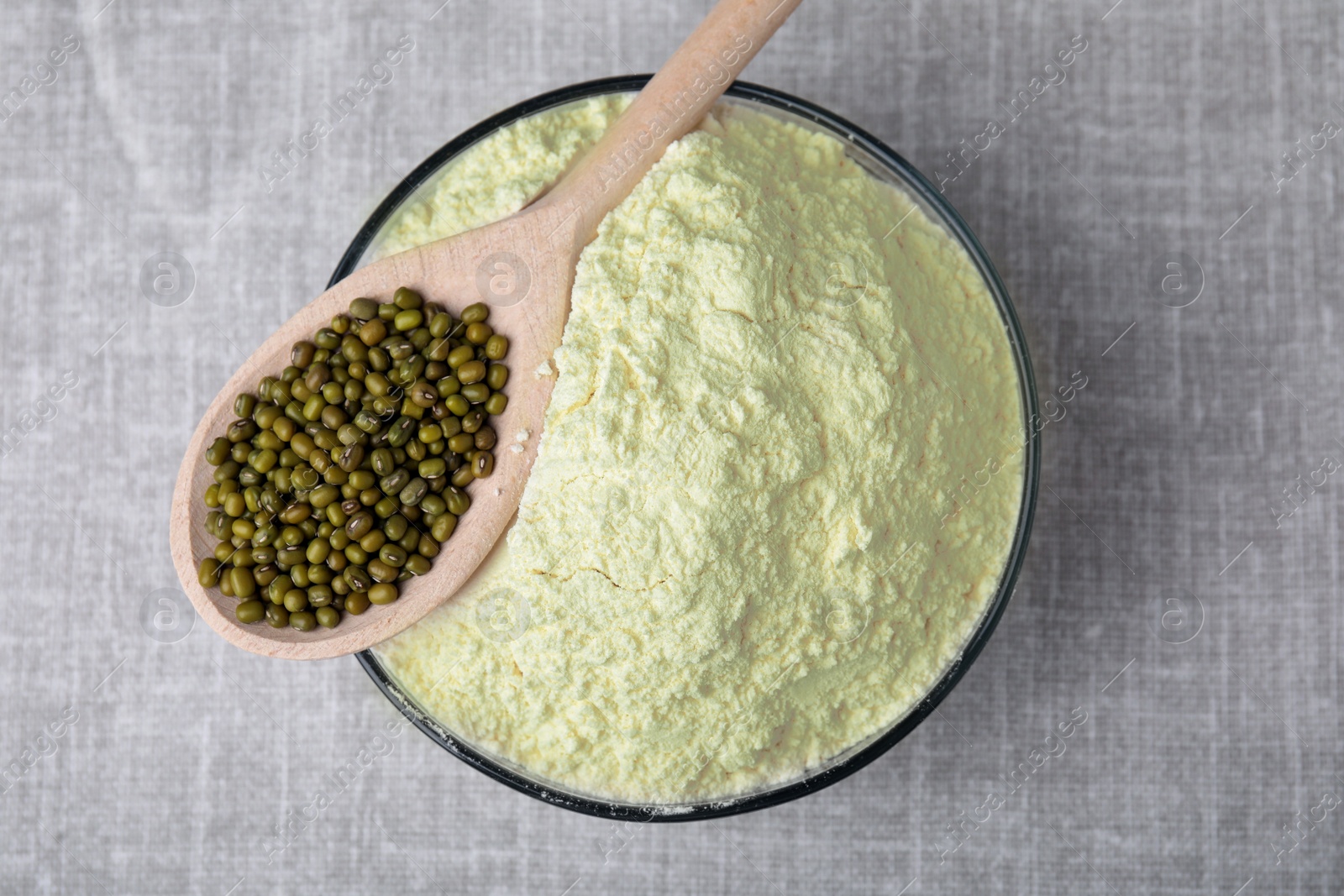 Photo of Bowl of flour, spoon and mung beans on light grey cloth, top view