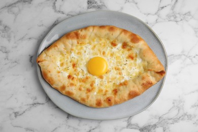 Fresh homemade khachapuri with cheese and egg on white marble table, top view