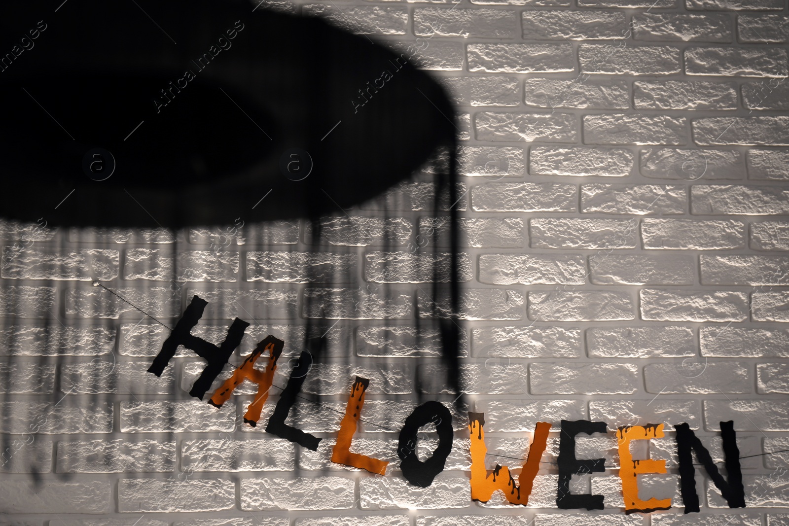 Photo of Word Halloween made of colorful letters and festive decor on brick wall. Space for text