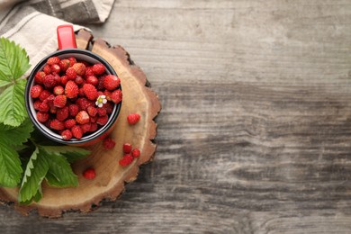 Fresh wild strawberries in mug and leaves on wooden table, top view. Space for text