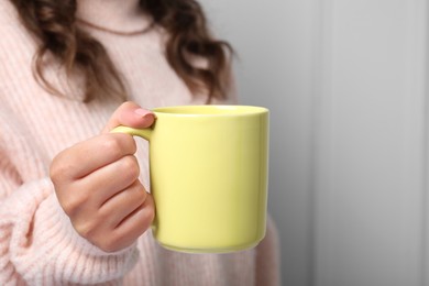 Photo of Woman holding yellow mug on light background, closeup. Mockup for design