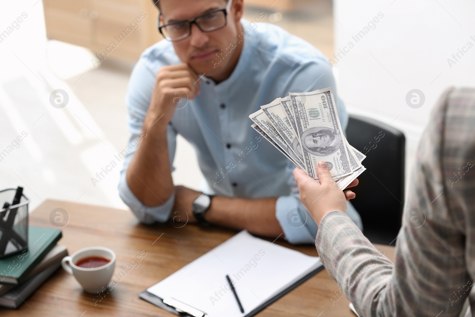 Photo of Woman offering bribe money to man at table, closeup