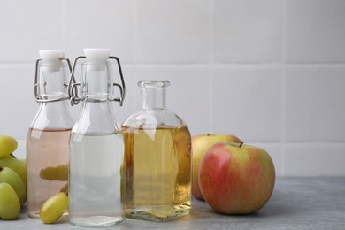 Different types of vinegar and fresh fruits on grey table