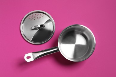 Photo of Empty steel saucepan and lid on dark pink background, flat lay