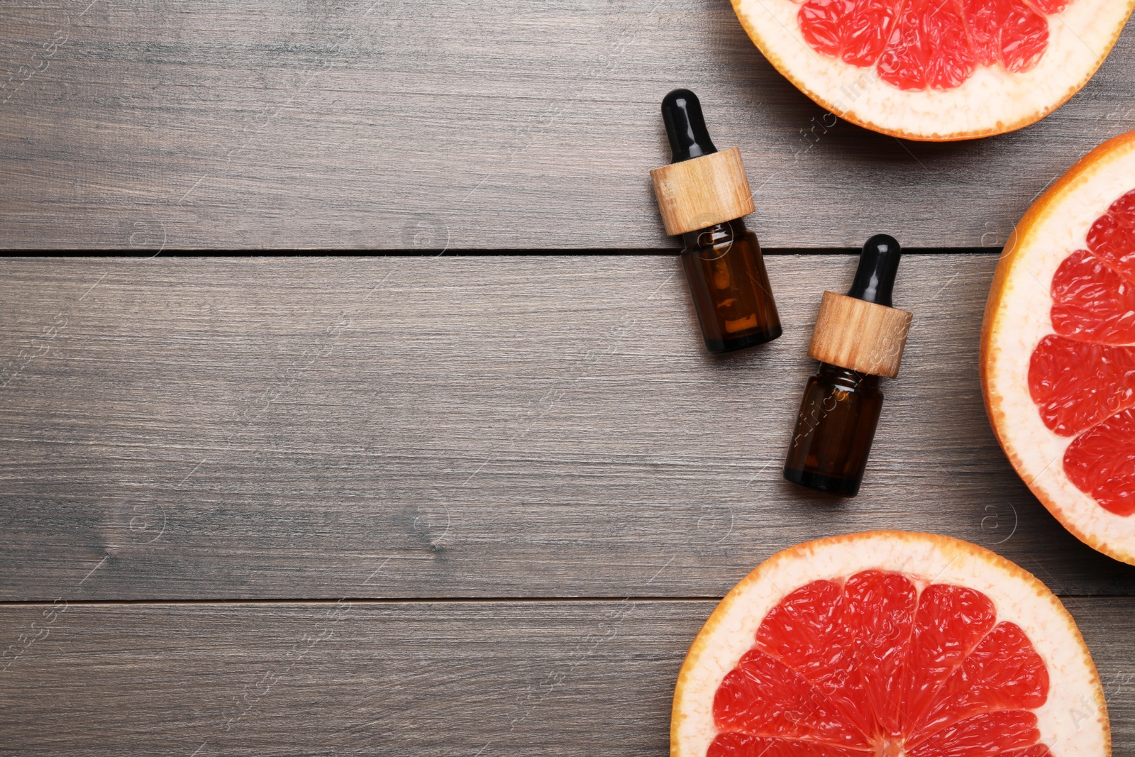 Photo of Bottles of citrus essential oil and grapefruit slices on wooden table, flat lay. Space for text