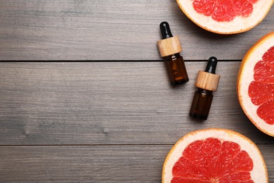 Bottles of citrus essential oil and grapefruit slices on wooden table, flat lay. Space for text