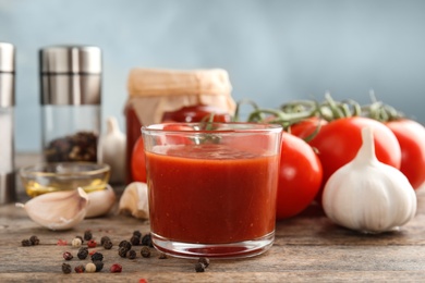 Photo of Composition with glass of tasty tomato sauce on wooden table against color background