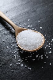 Photo of Organic white salt and spoon on black table, closeup