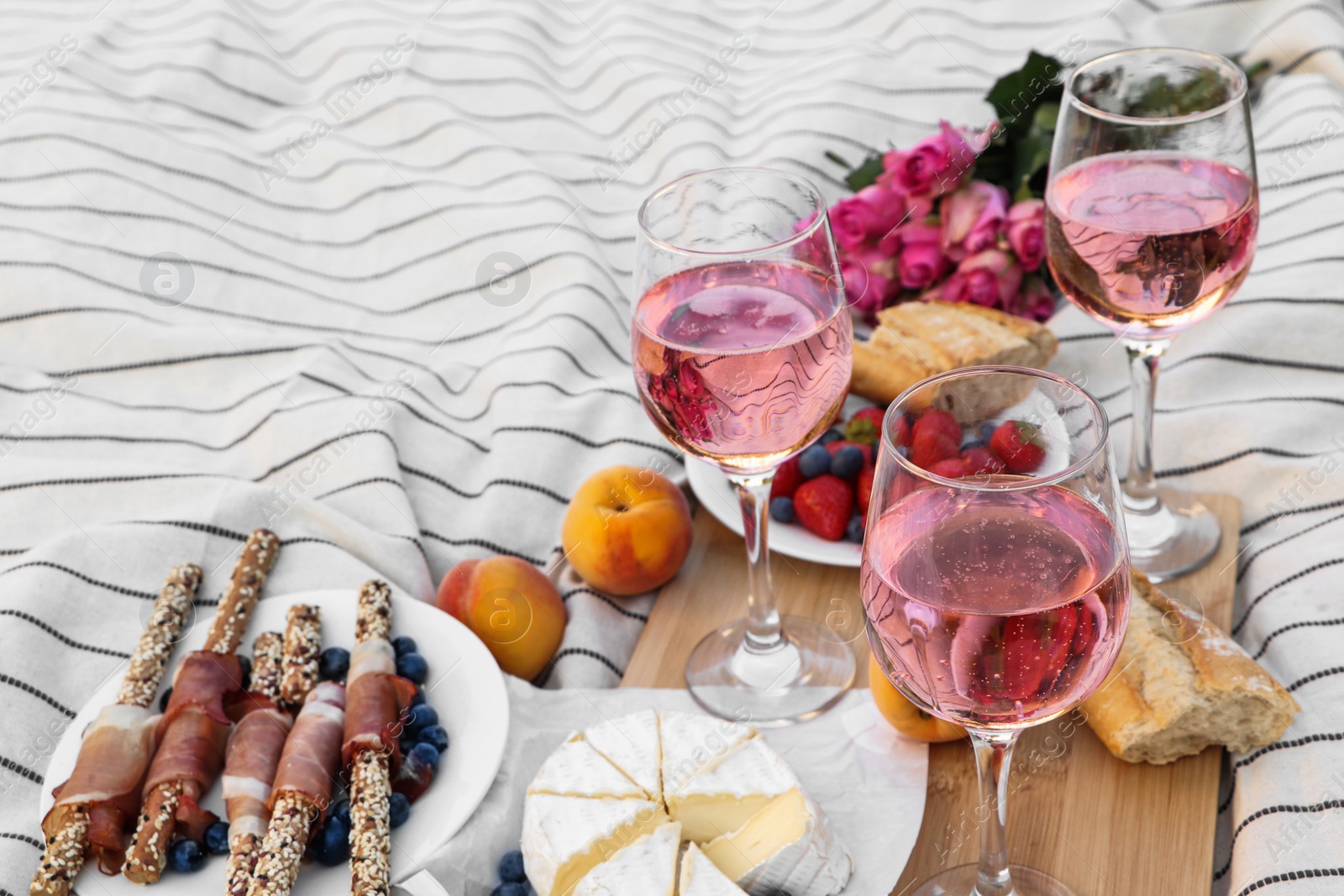 Photo of Glasses of delicious rose wine, flowers and food on white picnic blanket