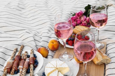 Photo of Glasses of delicious rose wine, flowers and food on white picnic blanket