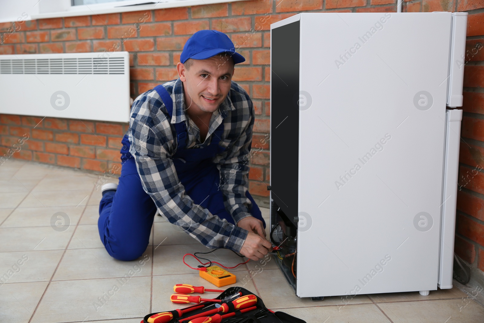 Photo of Male technician in uniform repairing refrigerator indoors