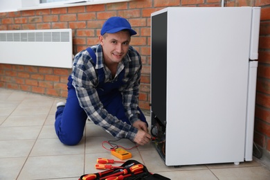 Male technician in uniform repairing refrigerator indoors