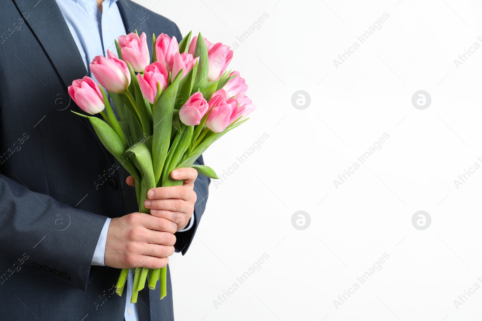 Photo of Man in elegant suit holding bouquet of beautiful spring tulips on light background, closeup. International Women's Day