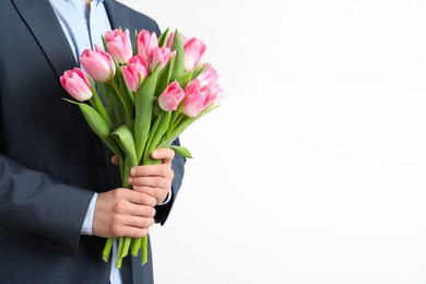 Photo of Man in elegant suit holding bouquet of beautiful spring tulips on light background, closeup. International Women's Day