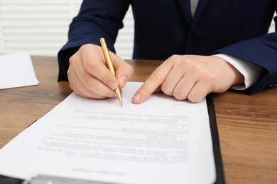 Photo of Man signing document at wooden table, closeup