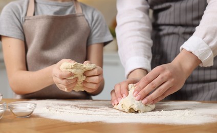 Photo of Making bread. Mother and her daughter kneading dough at wooden table indoors, closeup
