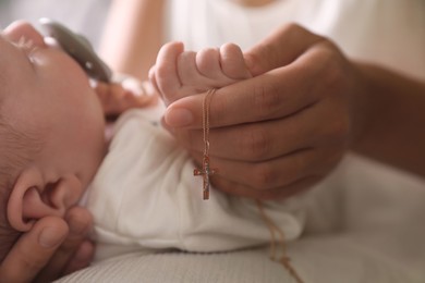 Photo of Mother holding Christian cross near newborn baby indoors, closeup