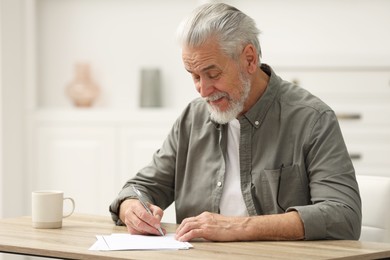 Photo of Senior man signing Last Will and Testament at table indoors. Space for text