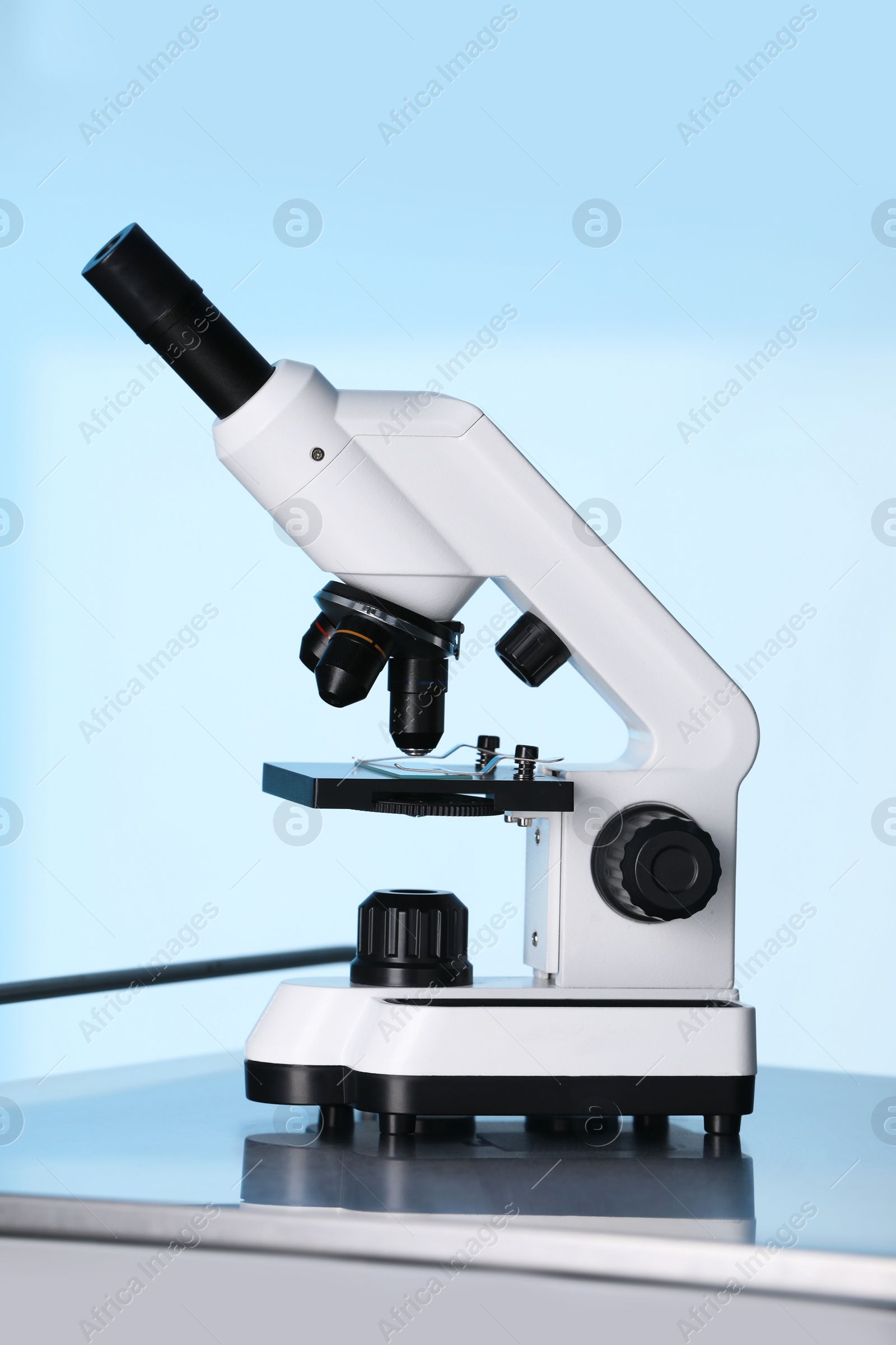 Photo of Modern microscope on metal table against light blue background