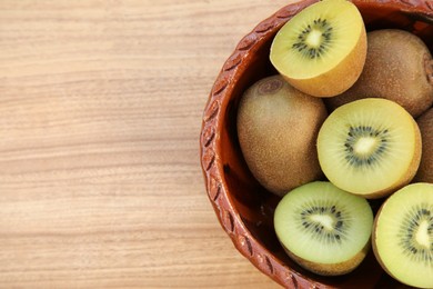 Photo of Bowl of many whole and cut fresh kiwis on wooden table, top view. Space for text