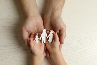 Father and child holding paper cutout of family at white wooden table, top view