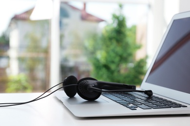 Photo of Modern laptop and headset on table indoors. Technical support concept