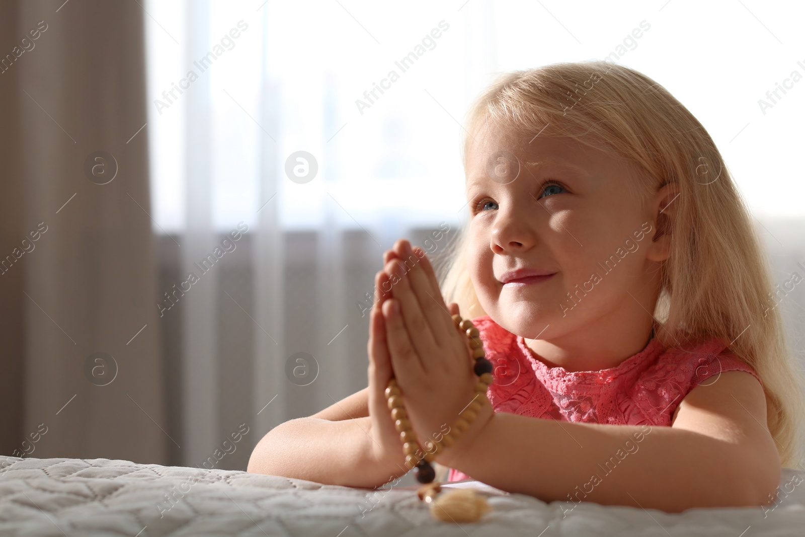 Photo of Cute little girl with beads praying in bedroom. Space for text